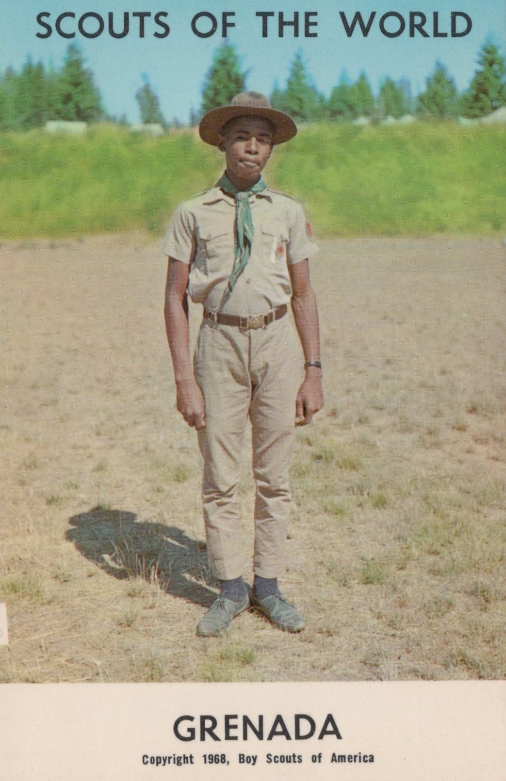 Scout in uniform standing in a field with 'Scouts of the World Grenada' text at the top.