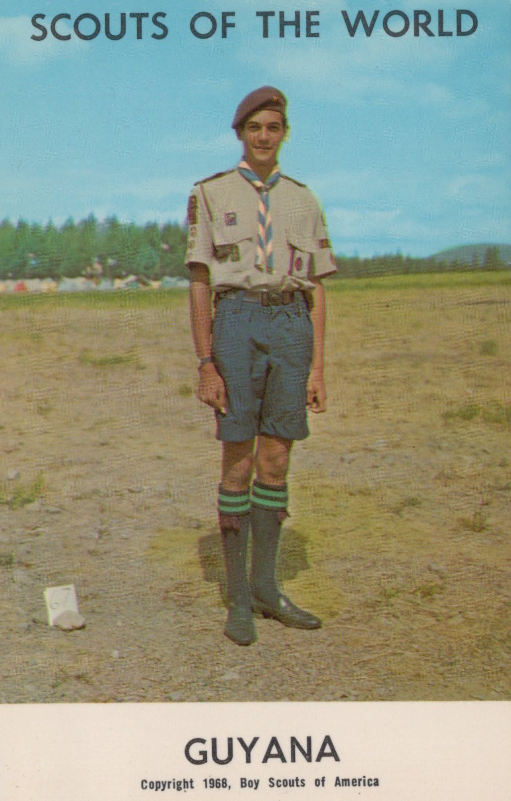Scout in uniform standing in an open field with 'Scouts of the World Guyana' text at the top.