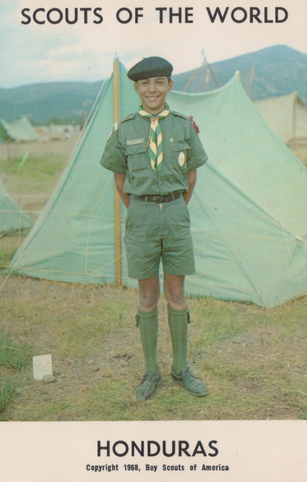 Scout in uniform standing in front of tents with 'Scouts of the World' and 'Honduras' text.