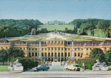 Large classical building with a garden and statues, vintage cars in front