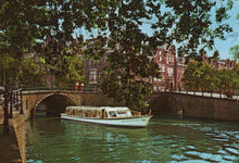 Load image into Gallery viewer, Boat on a canal with historic buildings and trees in the background

