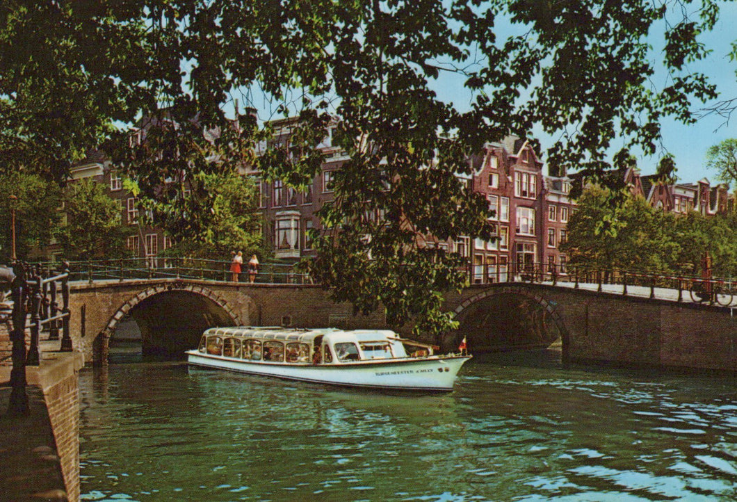 Boat on a canal with historic buildings and trees in the background