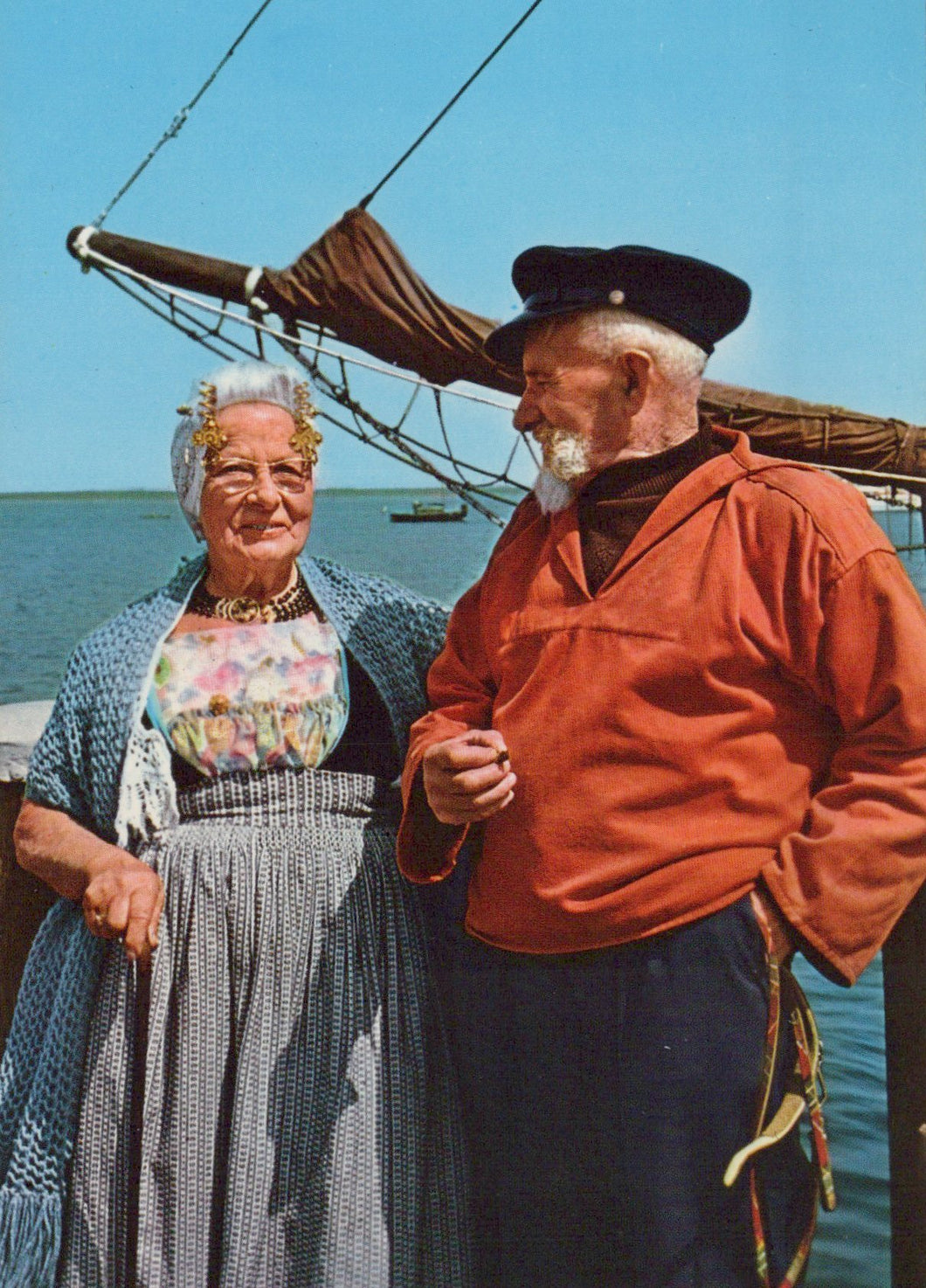 Two people standing on a dock with a sailboat in the background