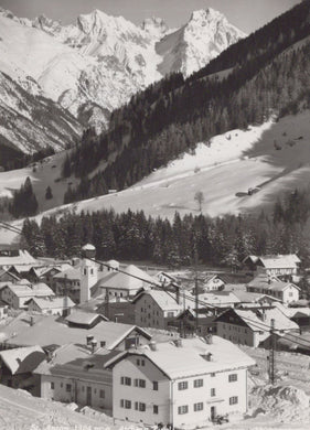 Vintage black and white photograph of a mountain village with snow-capped peaks.