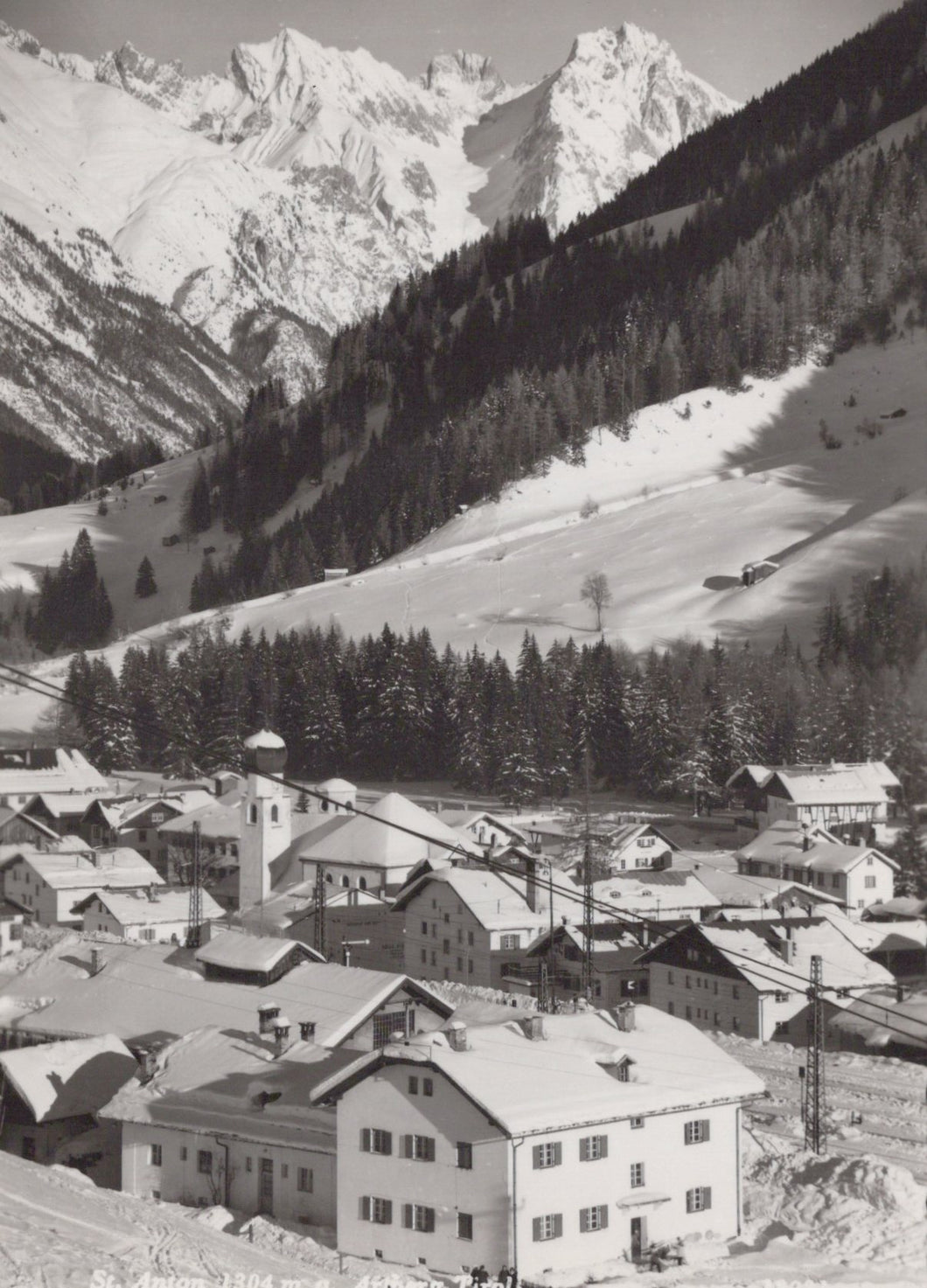 Vintage black and white photograph of a mountain village with snow-capped peaks.