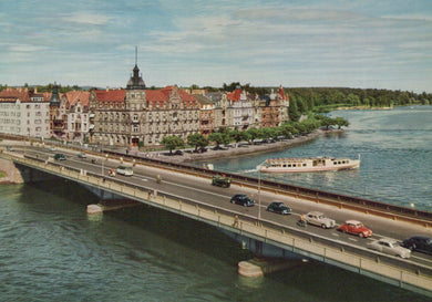 Bridge over a river with cars and a boat, buildings on the opposite bank