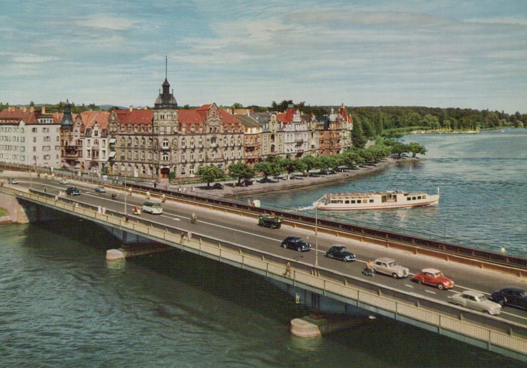 Bridge over a river with cars and a boat, buildings on the opposite bank