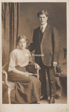 Vintage photograph of a man and woman posing together in formal attire against a curtain backdrop.
