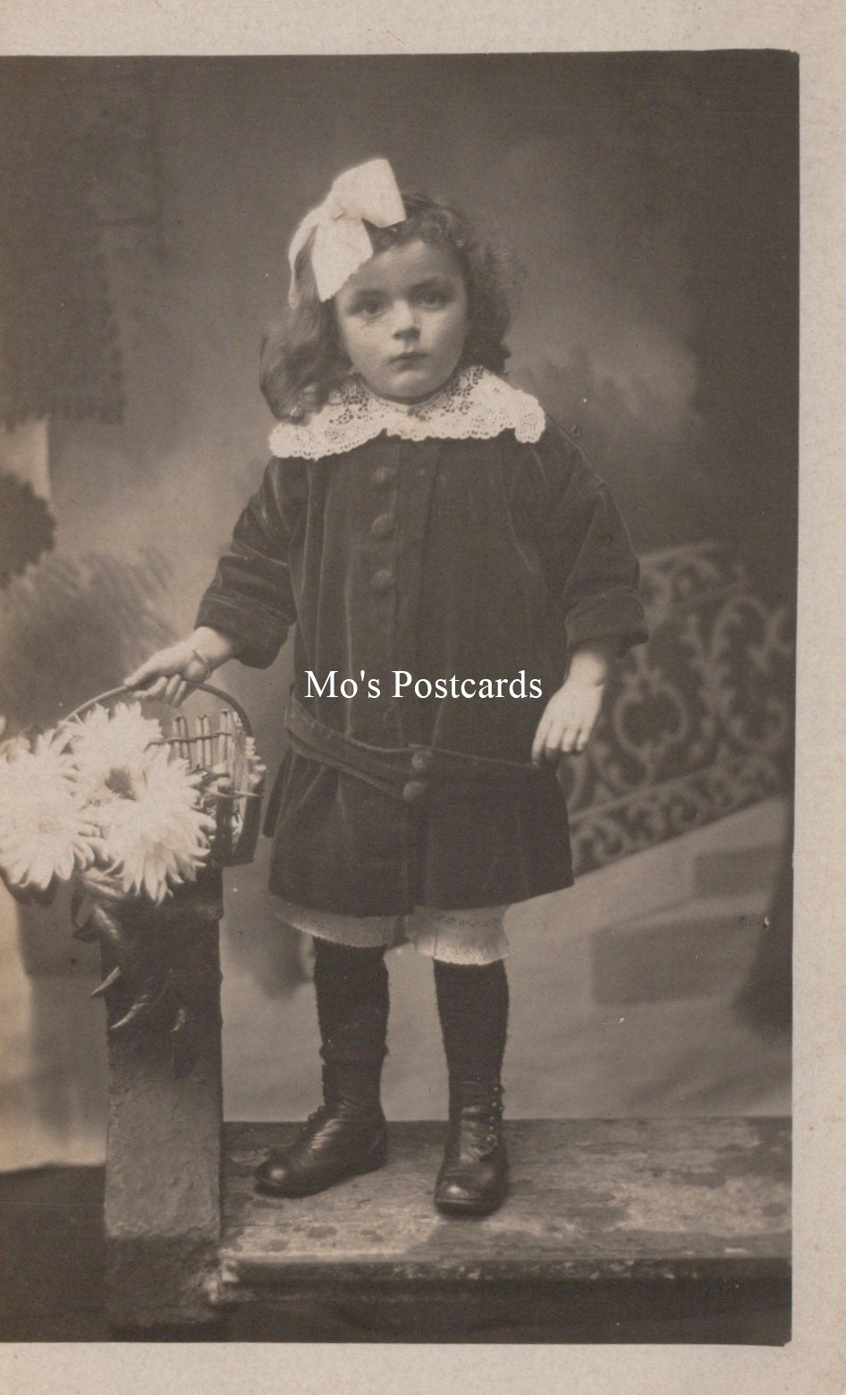 Vintage photograph of a young girl in formal attire with a decorative bow, labeled 'Mo's Postcards'.