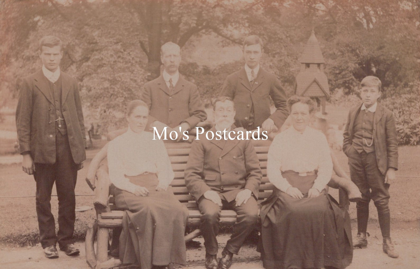 Vintage sepia-toned photograph of a group of people sitting on a bench outdoors.
