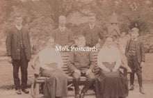 Load image into Gallery viewer, Vintage sepia-toned photograph of a group of people sitting on a bench outdoors.
