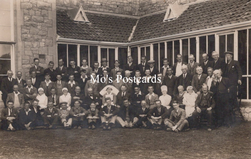 Vintage black and white photo of a group of people sitting outside a building with 'Mo's Postcards' text overlay.