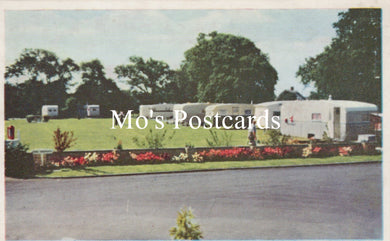 Vintage-style postcard with a caravan park scene, featuring greenery and floral borders.
