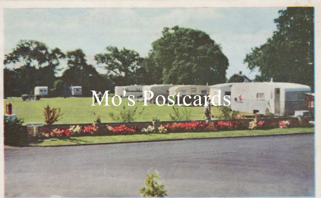 Vintage-style postcard with a caravan park scene, featuring greenery and floral borders.