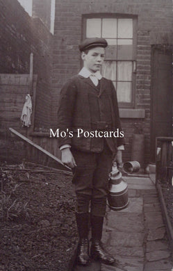 Vintage black and white photo of a boy holding a water jug in front of a brick building.