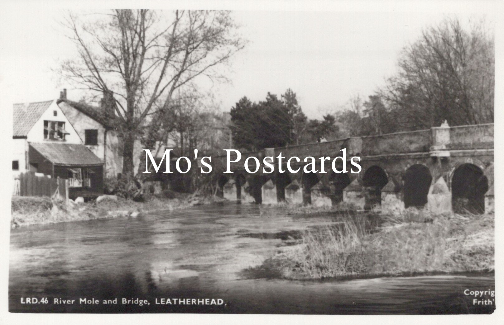 Vintage black and white postcard of a bridge over a river with trees and buildings in the background 
