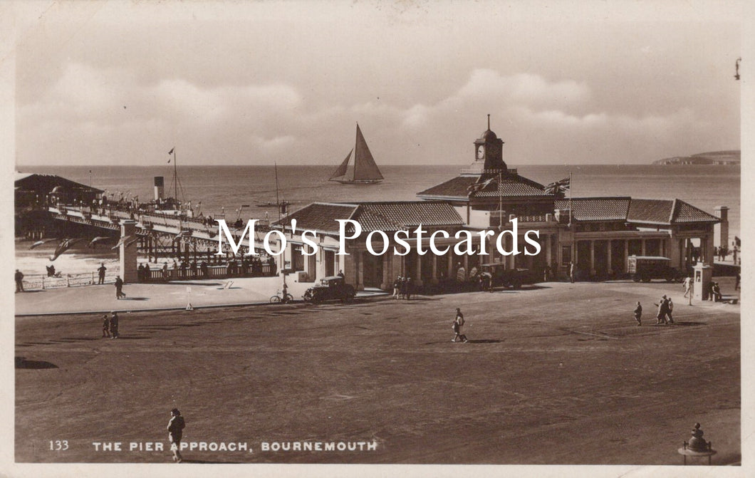 Vintage black and white postcard of a pier approach with a sailboat and buildings.
