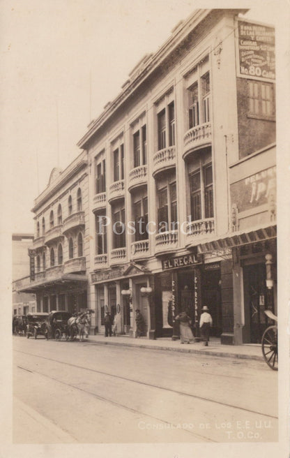 Vintage black and white photo of a street scene with a building and people on a sidewalk.