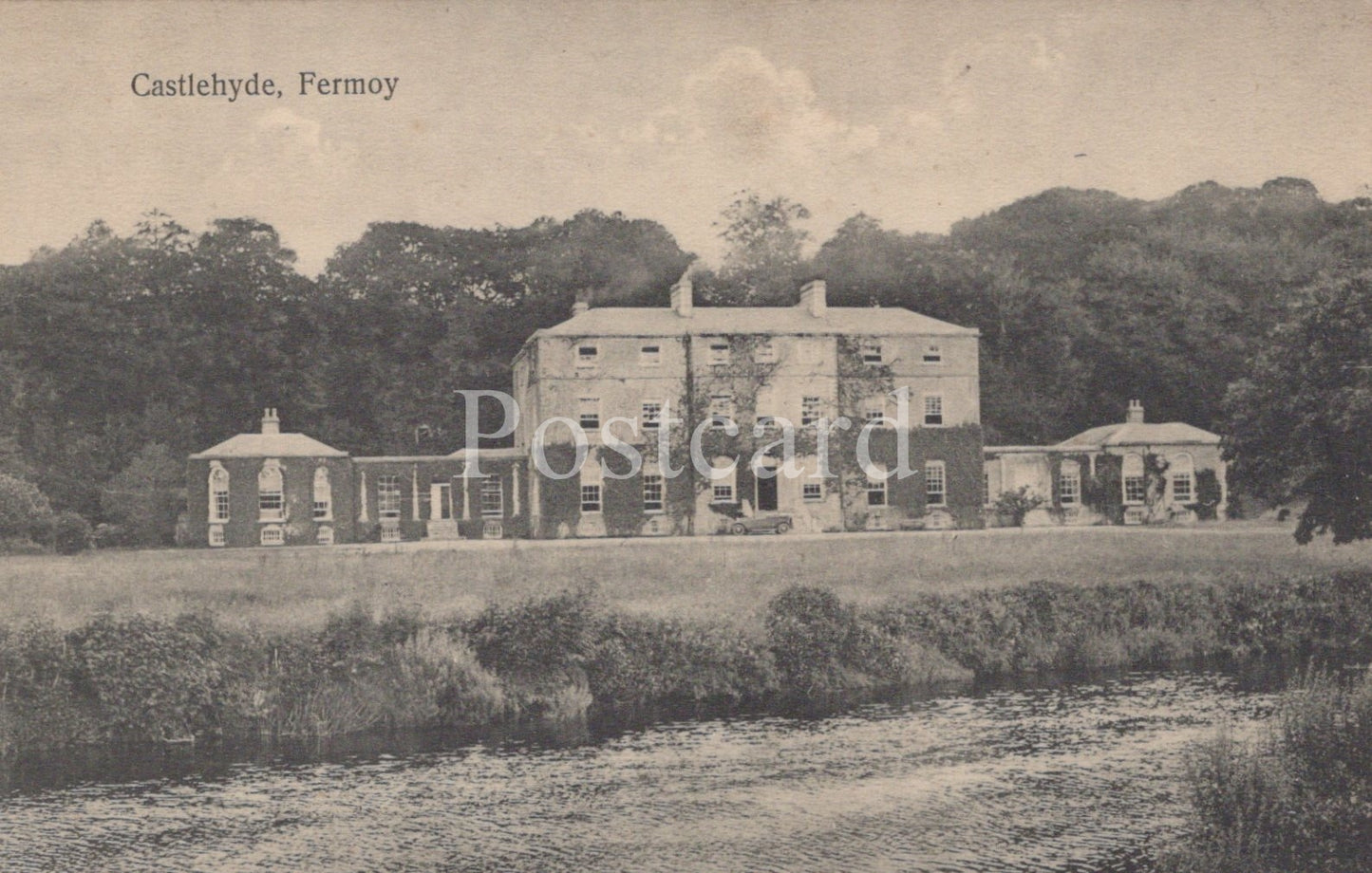 Vintage black and white postcard of a large house with trees and grass in the foreground.