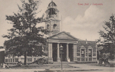 Vintage black and white photograph of a town hall building with clock tower and cannons in front.