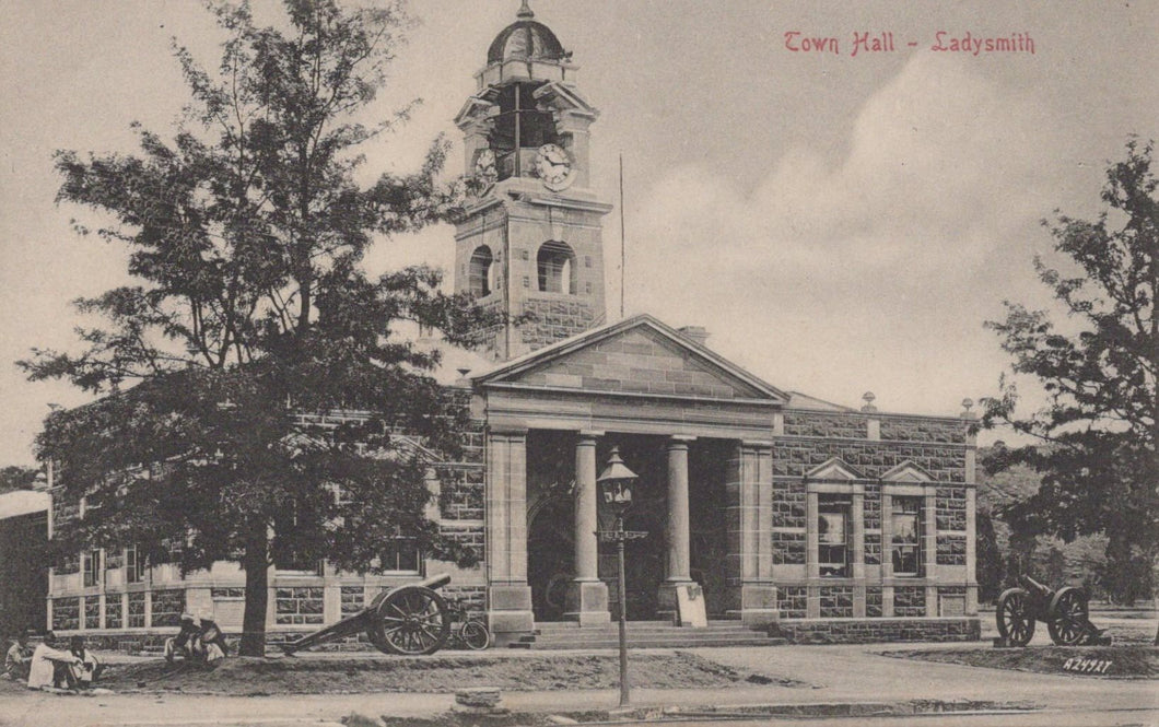Vintage black and white photograph of a town hall building with clock tower and cannons in front.