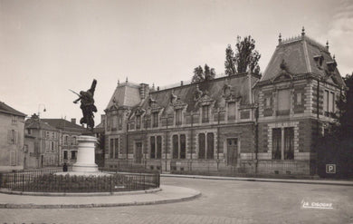 Historical black and white photo of a building with a statue in front