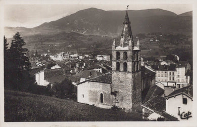 Vintage black and white photo of a town with a prominent clock tower and mountains in the background.