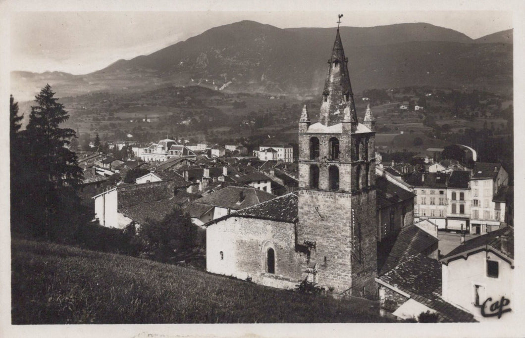 Vintage black and white photo of a town with a prominent clock tower and mountains in the background.