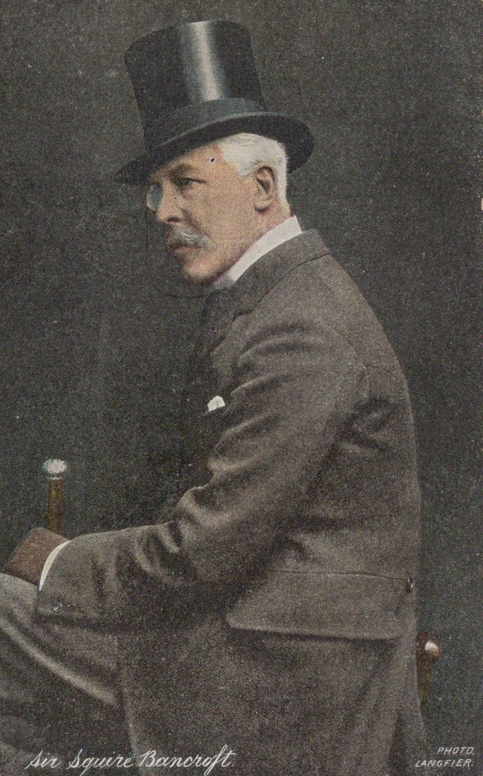 Man in formal attire with a top hat and smoking a pipe, sitting.