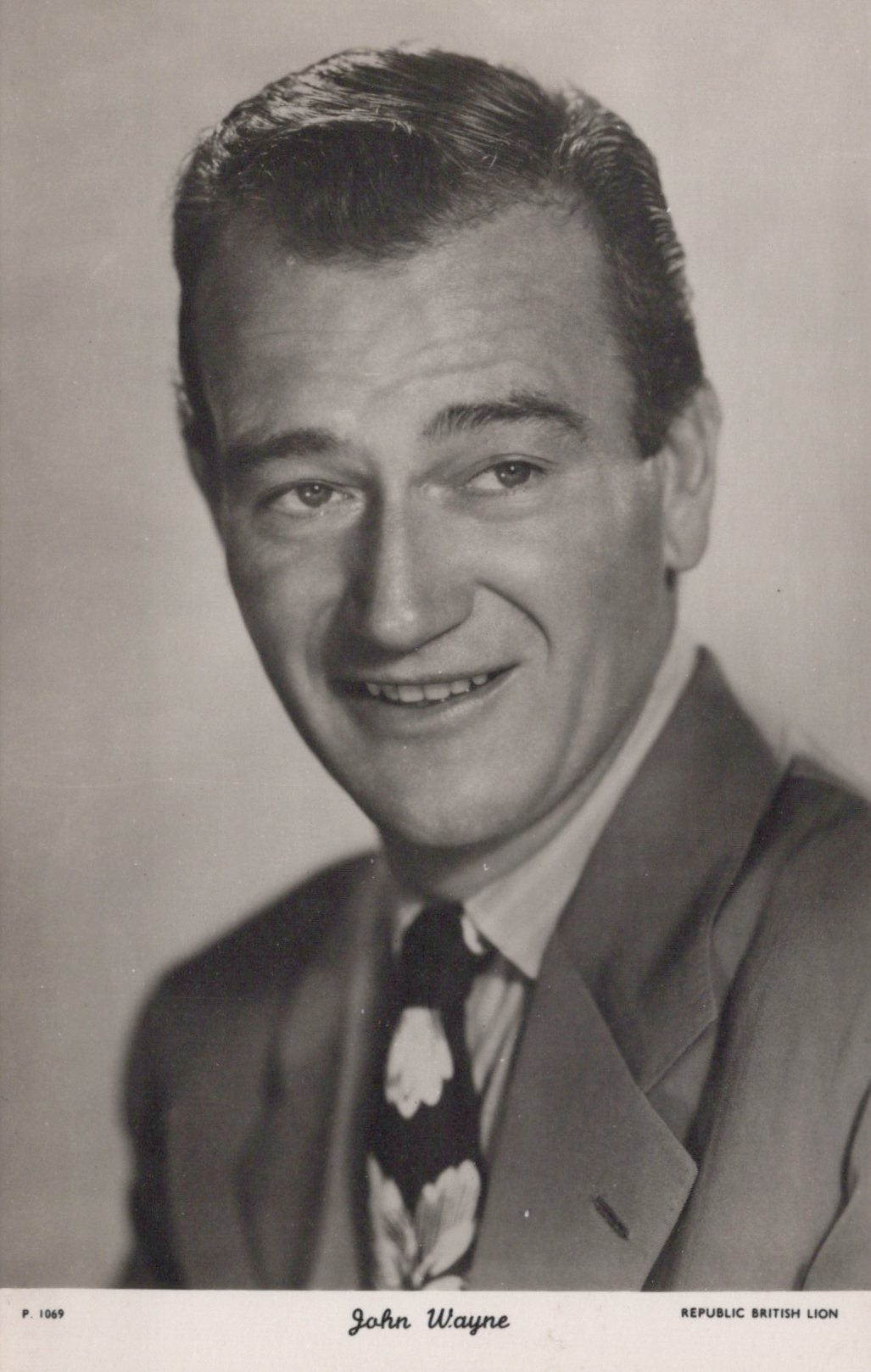 Black and white portrait of a smiling man in a suit with a Republic British Lion logo.