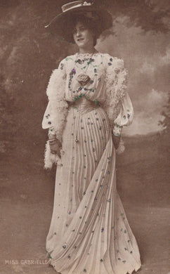 Vintage photograph of a woman in an elaborate dress with floral details against a cloudy sky.
