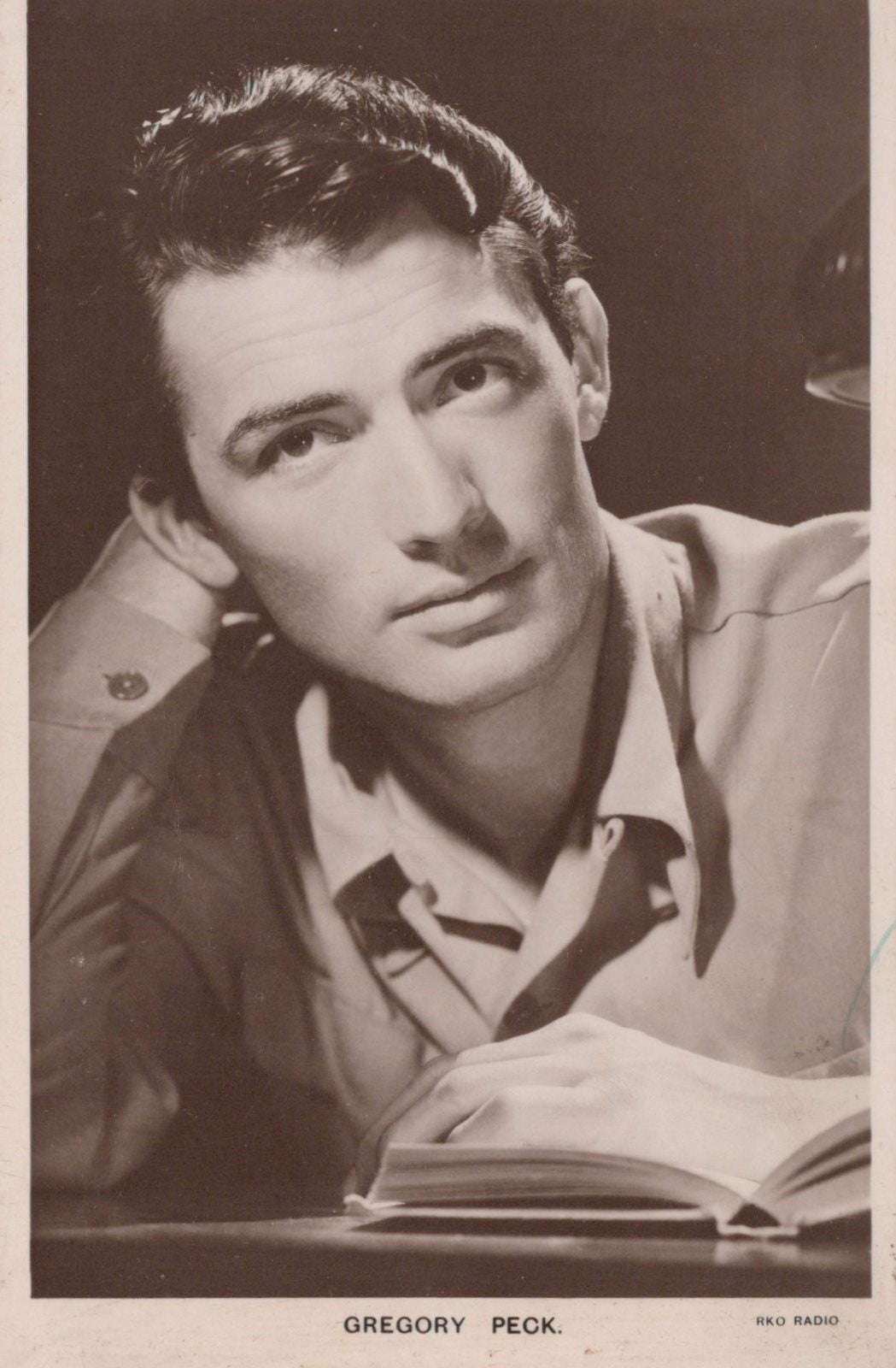 Vintage photograph of a man sitting at a desk with an open book, wearing a light-colored shirt.
