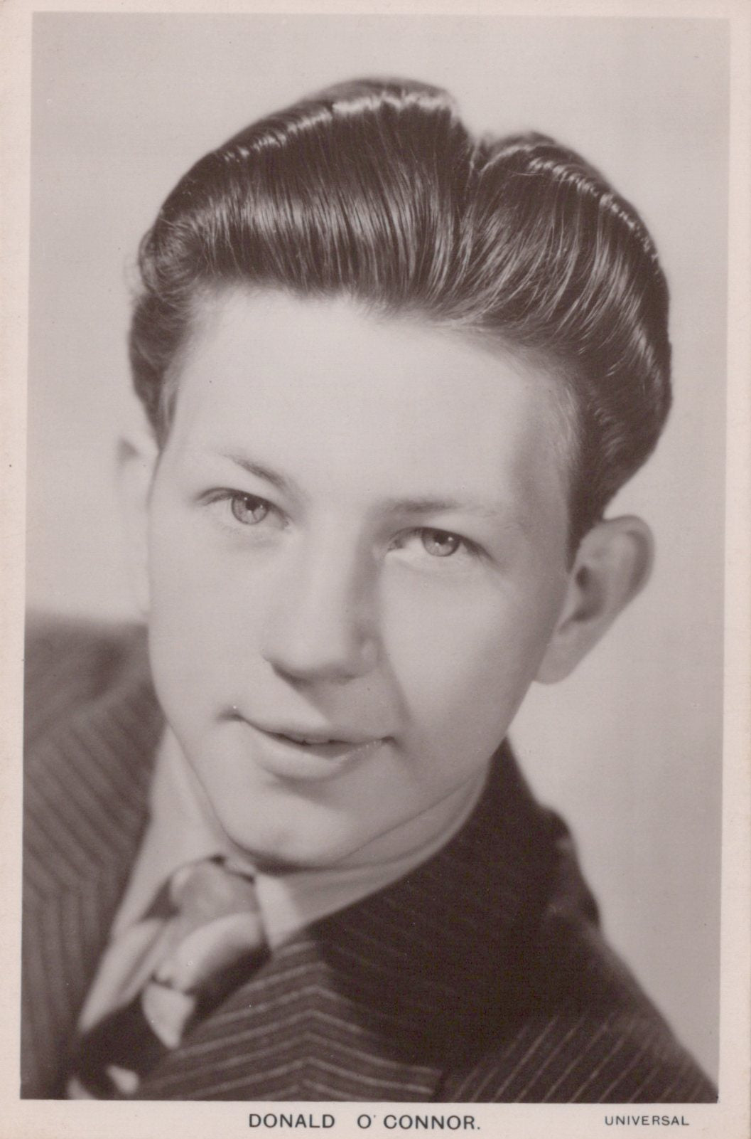 Vintage black and white portrait of a man with styled hair, wearing a suit.