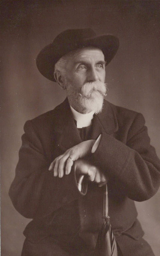 Black and white portrait of a man wearing a hat and coat, holding an umbrella.