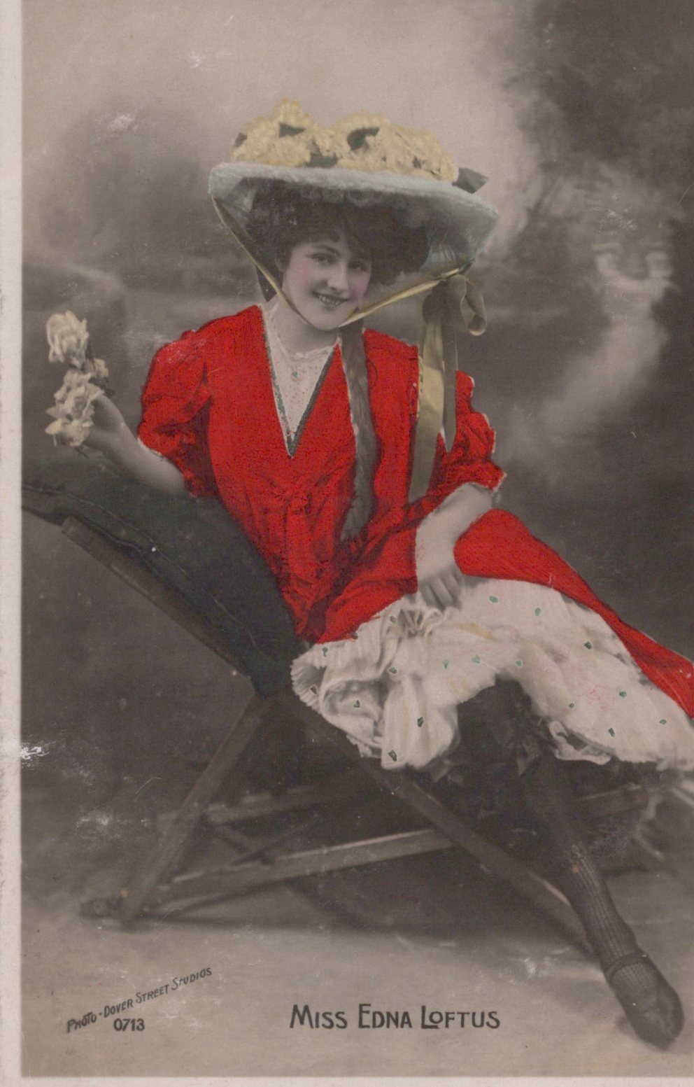 Woman in a red dress and large hat sitting on a bench, with 'Miss Eona Loftus' text.