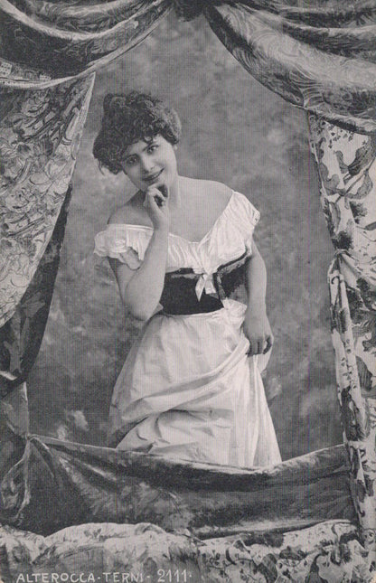 Vintage black and white photograph of a woman in a formal dress with decorative curtains.