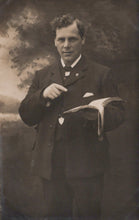 Load image into Gallery viewer, Man in formal attire holding a book against a dark background
