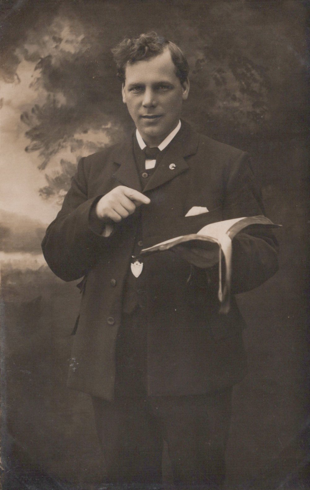 Man in formal attire holding a book against a dark background
