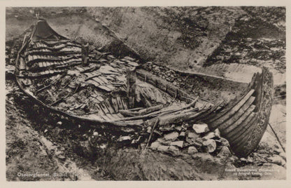 Wrecked wooden boat on a rocky shore with a small hut nearby.