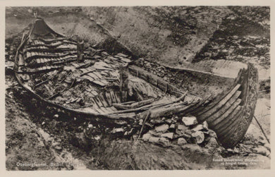 Wrecked wooden boat on a rocky shore with a small hut nearby.