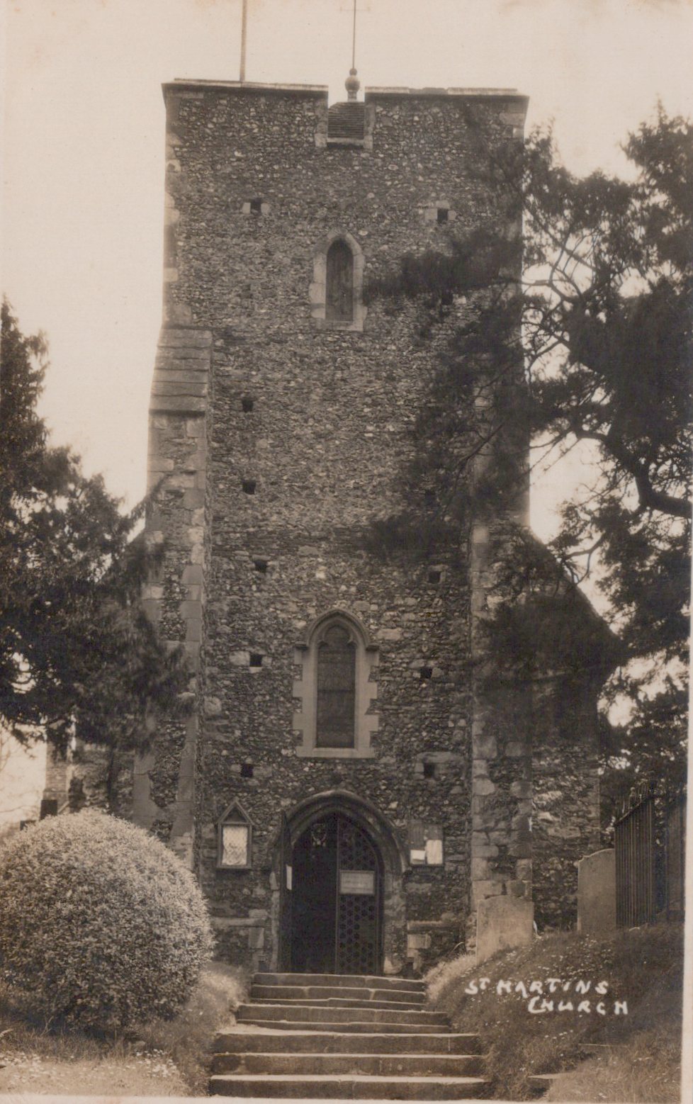 Vintage postcard of a church tower with steps leading up to it, surrounded by trees and shrubs.