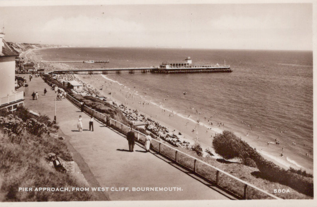 Vintage black and white photo of a beach scene with a pier and promenade.