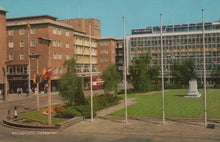 Load image into Gallery viewer, Vintage photograph of a city square with buildings, flags, and greenery.
