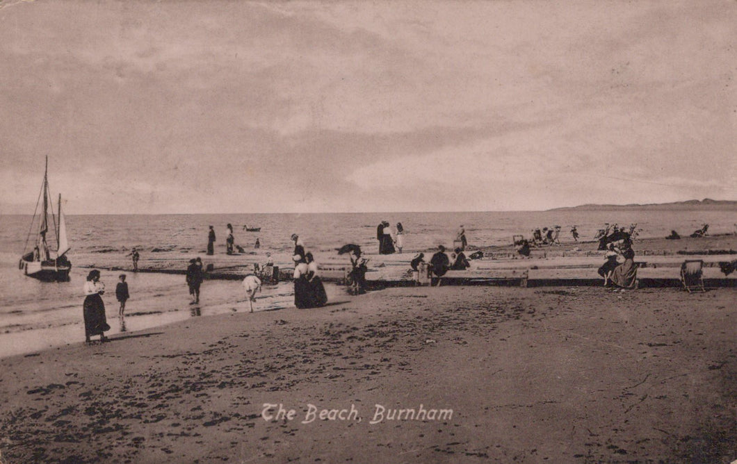 Vintage black and white postcard of a beach scene with people and boats.