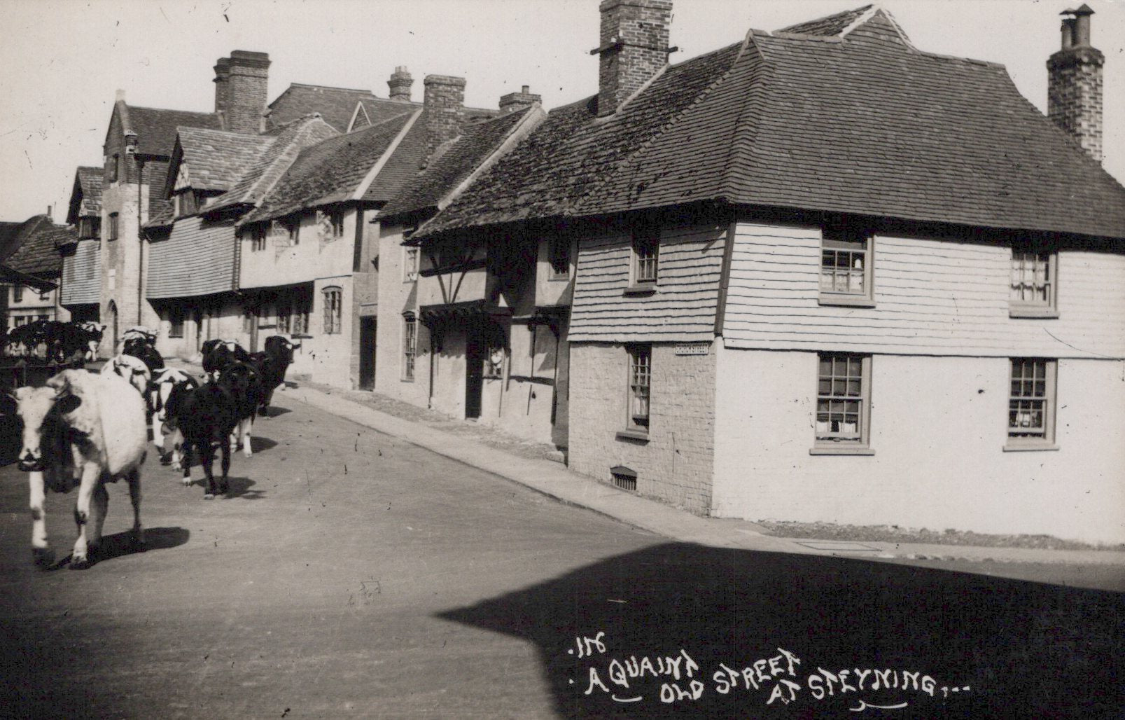 Vintage black and white photo of a quaint street with horse-drawn carriages and traditional buildings.