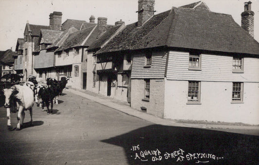 Vintage black and white photo of a quaint street with horse-drawn carriages and traditional buildings.