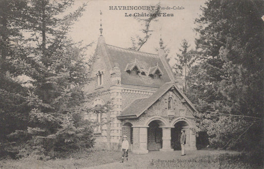 Vintage black and white photo of a stone building with a pointed roof, surrounded by trees.