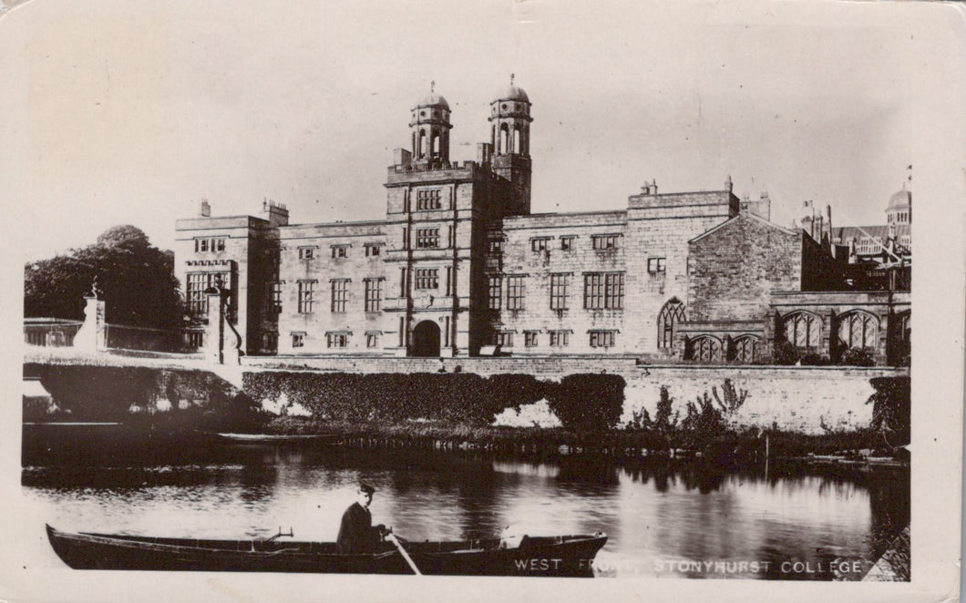 Historic black and white photo of a large building with a river and boat in front