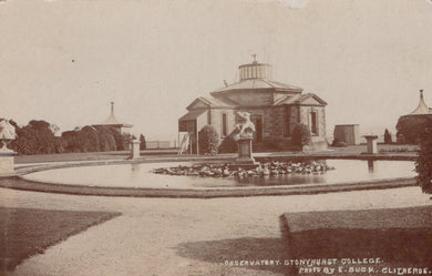Historical black and white photograph of a garden with a building and pond.