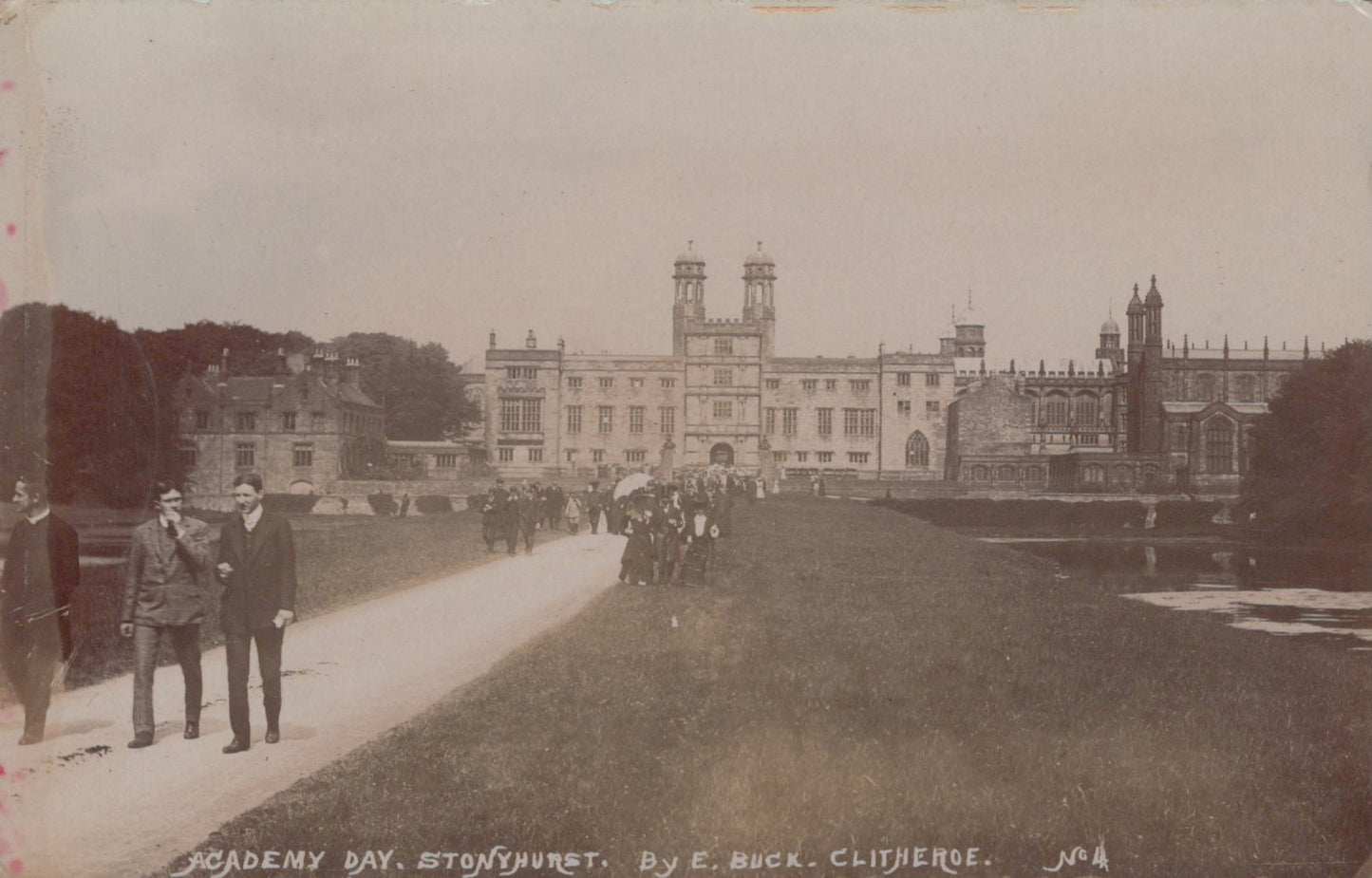 Vintage photograph of a large building with two men walking on a path in front.